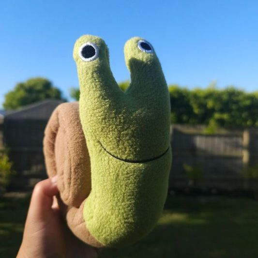 Close-up of the Snail Snuffle dog toy showing plush green snail head and brown spiral shell texture